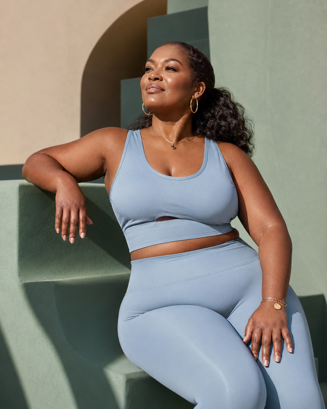 A confident woman in a soft blue set seated against a sage architectural background